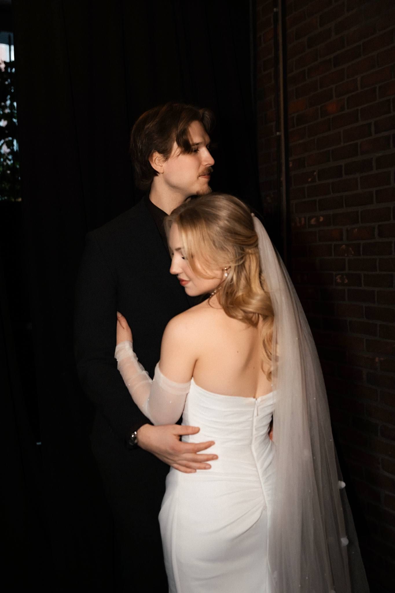 Couple standing close in a dark doorway, her veil trailing