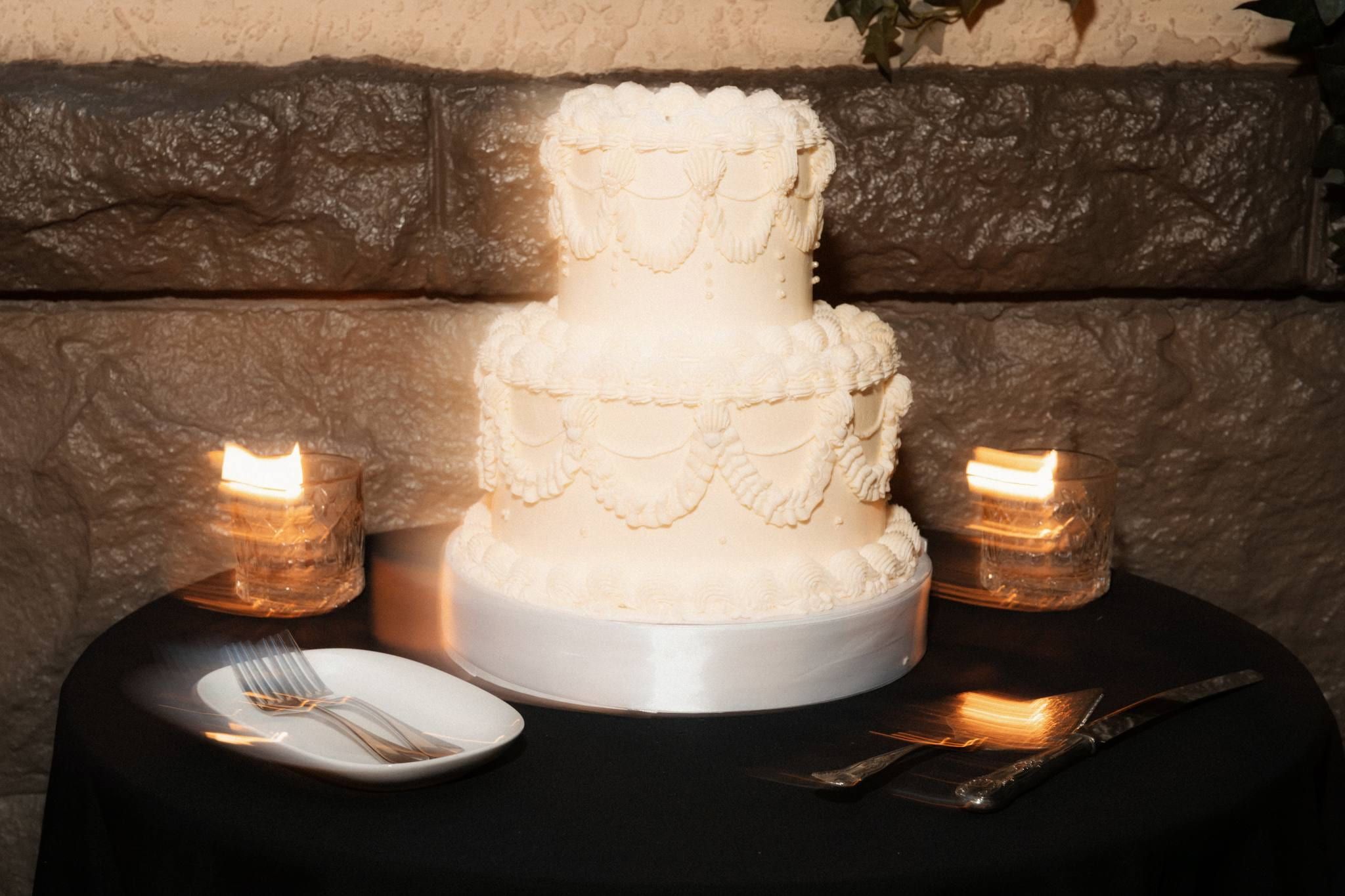 Tiered white wedding cake on a black table between candles