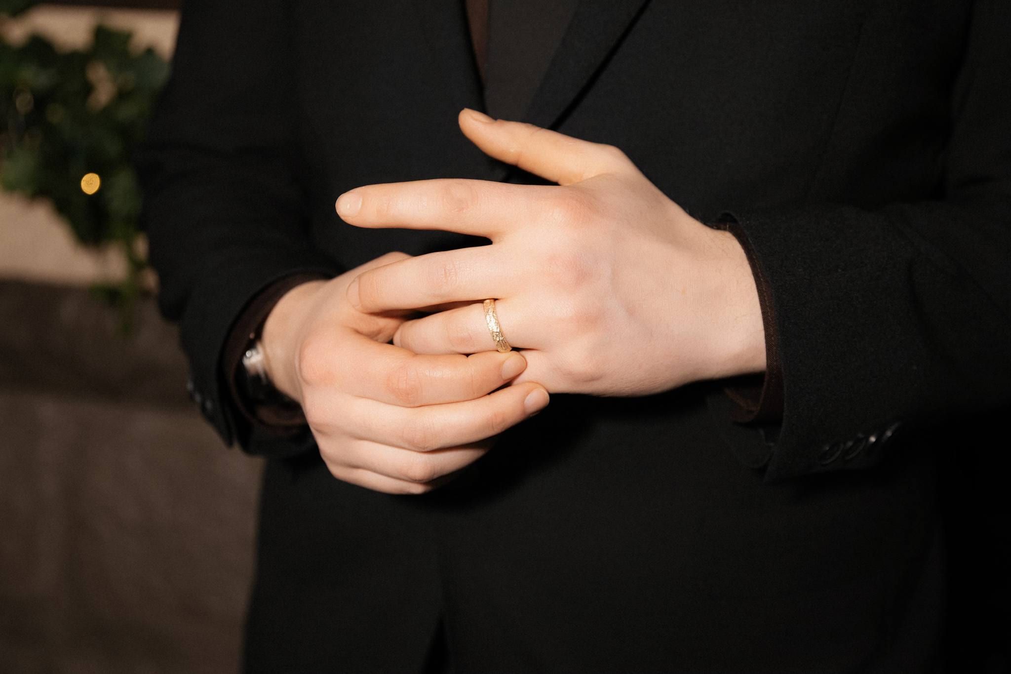 Close-up of the groom's clasped hands and wedding ring