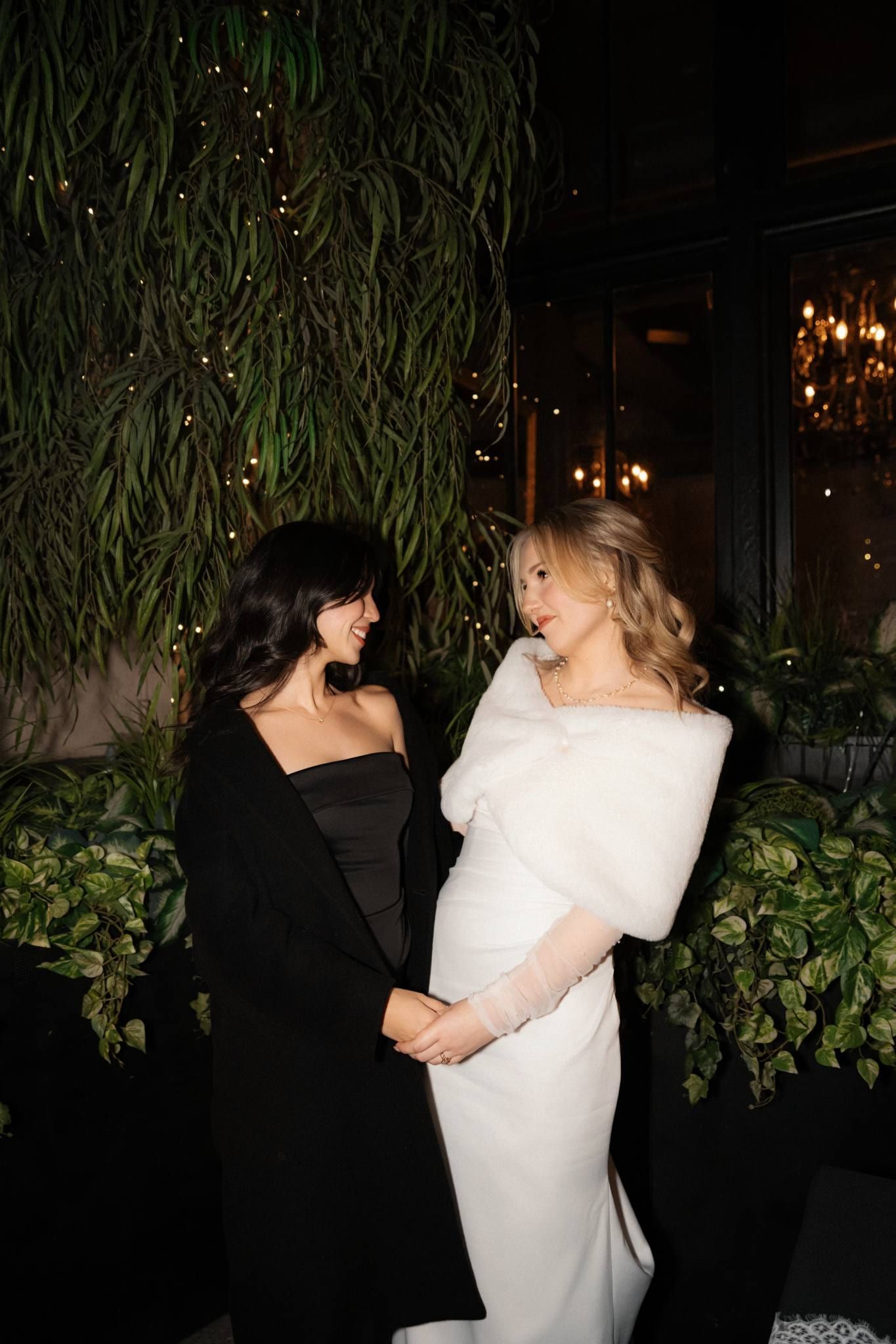 Bride laughing with her mother in a black dress before a green wall