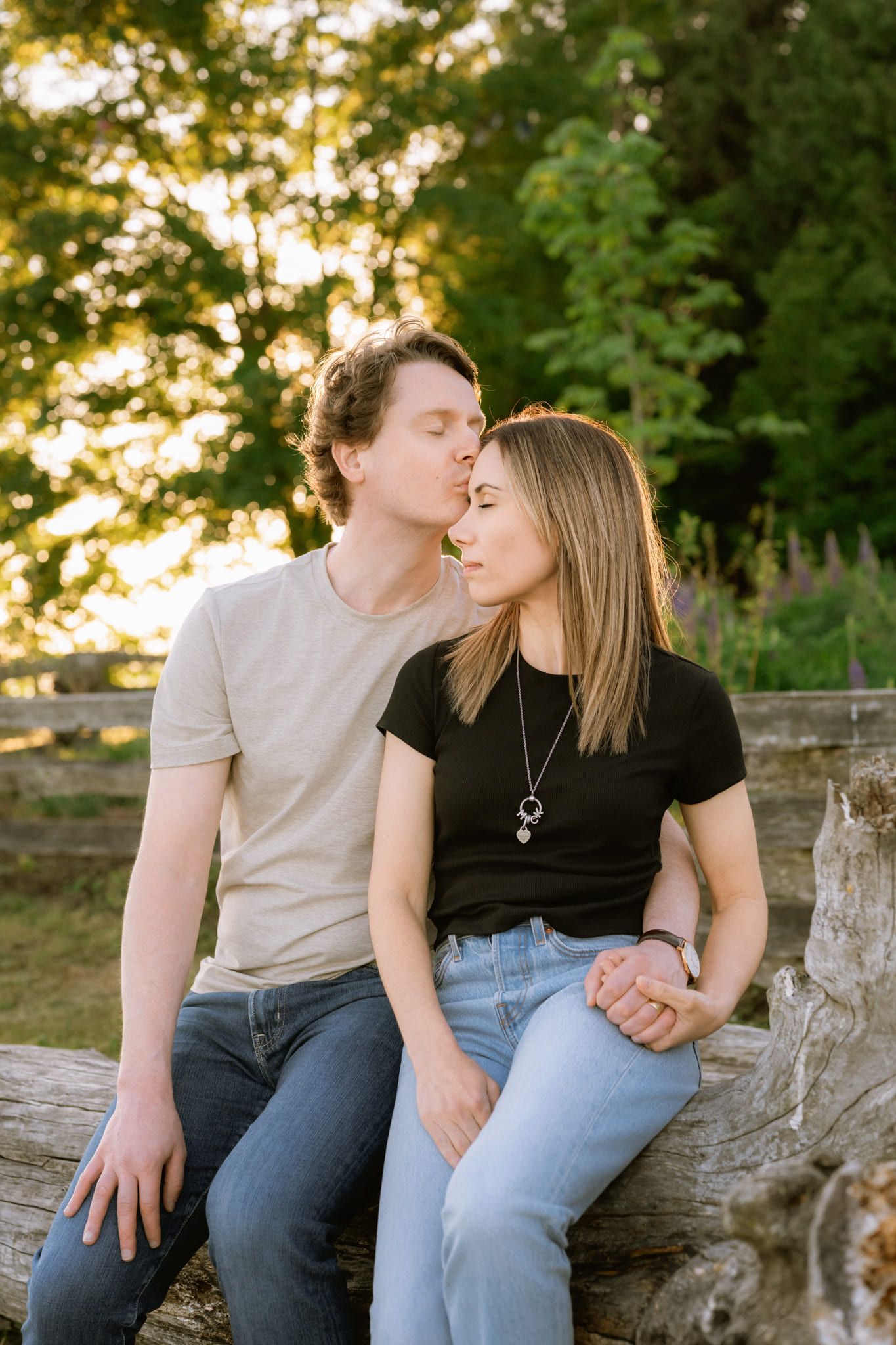 Engagement pics by the water, couple sharing a kiss on a driftwood log