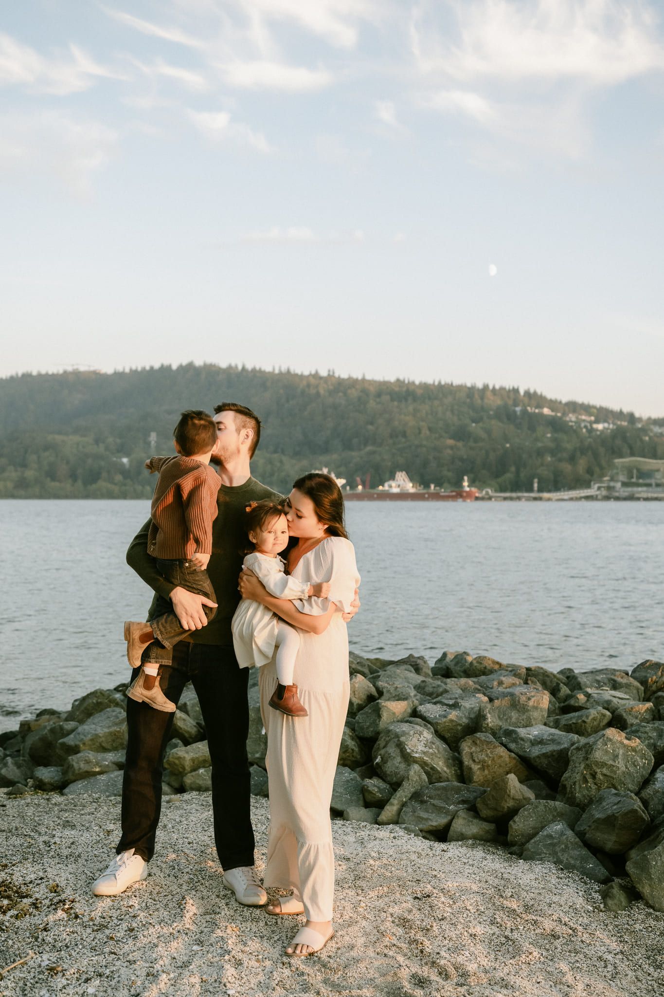 Creative family pictures by the water, parents holding their children on a rocky breakwater