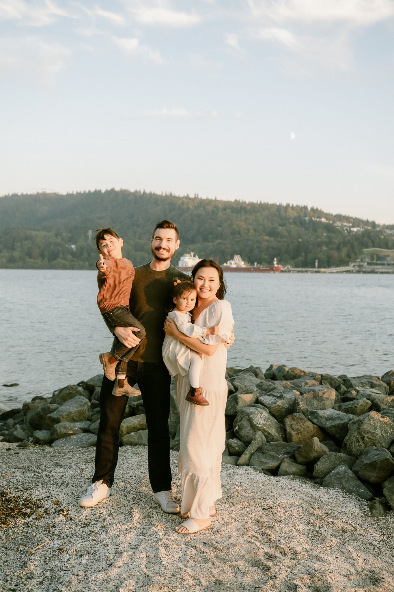 Natural family photography, parents holding their two children on the rocks by the water