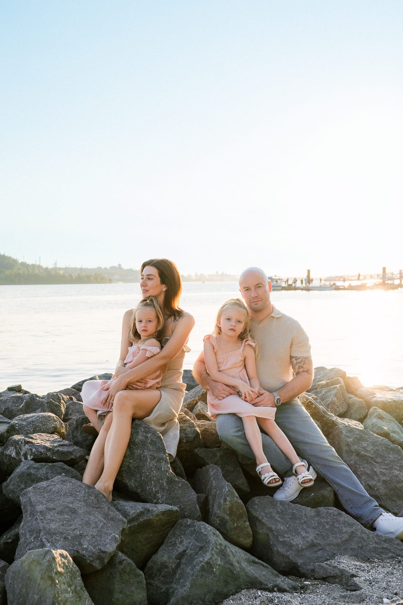Family photoshoot, family sitting on the rocks by the water in soft evening light