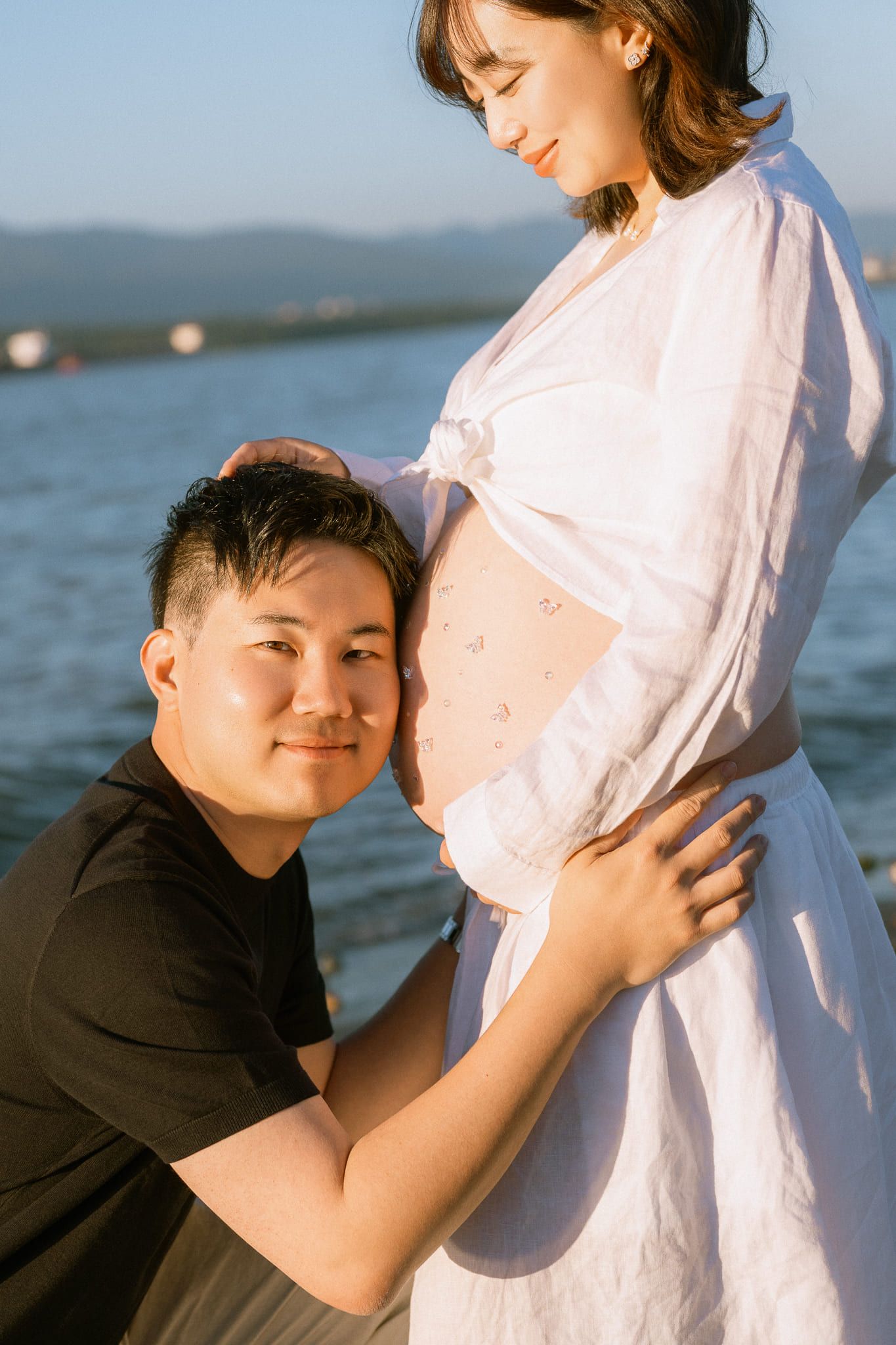 Maternity photoshoot by the water, dad-to-be holding his partner's bump