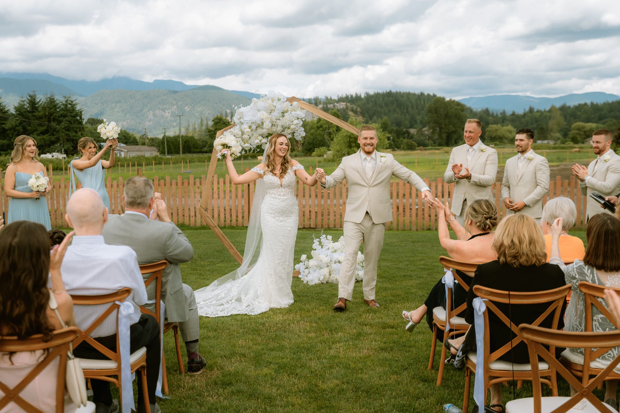 Outdoor wedding photos, bride celebrating down a grassy aisle as guests cheer