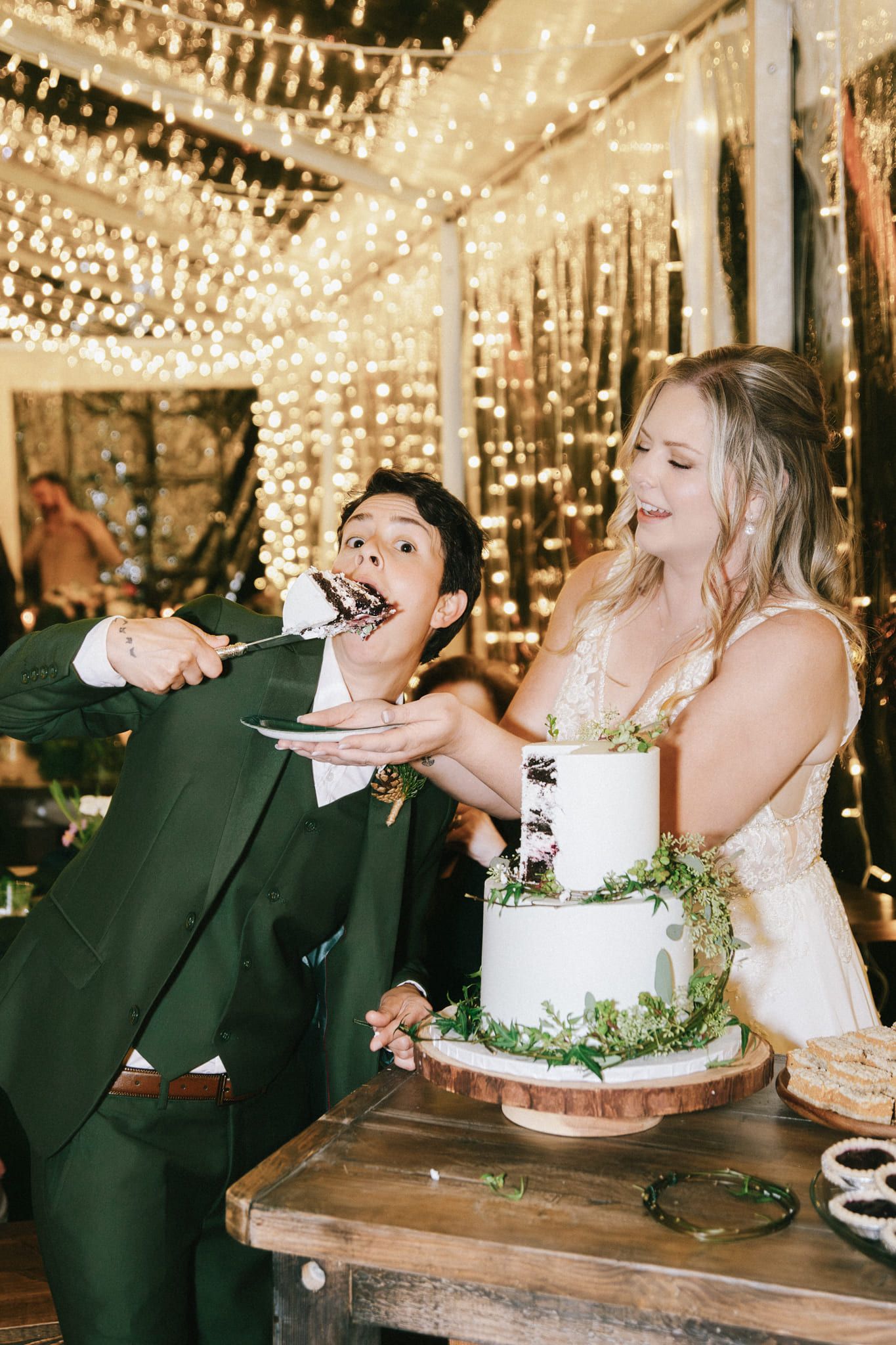 Intimate wedding photography under a canopy of fairy lights, bride and groom feeding each other cake