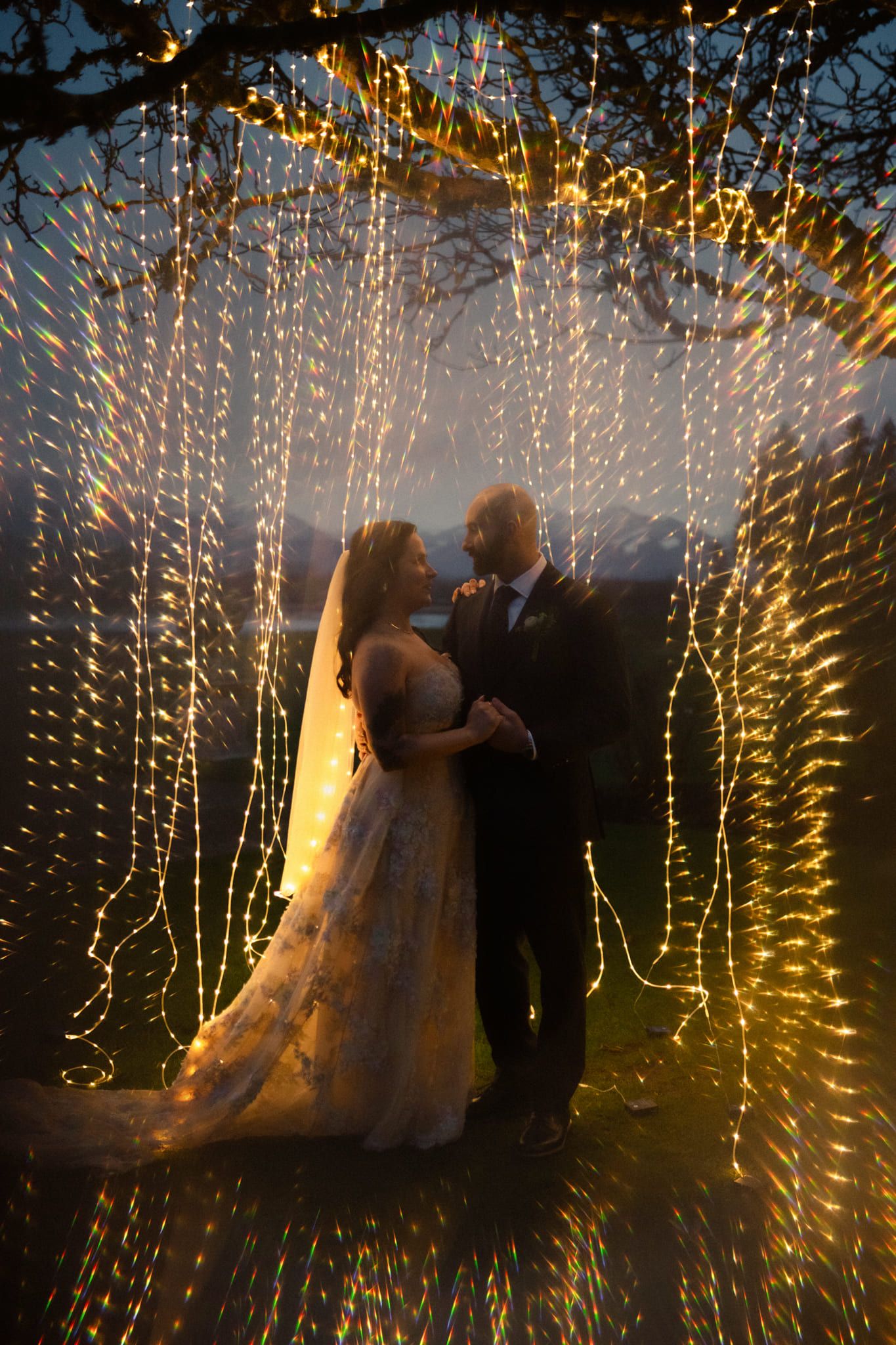 Indoor wedding photography, bride and groom embracing behind a curtain of string lights at night
