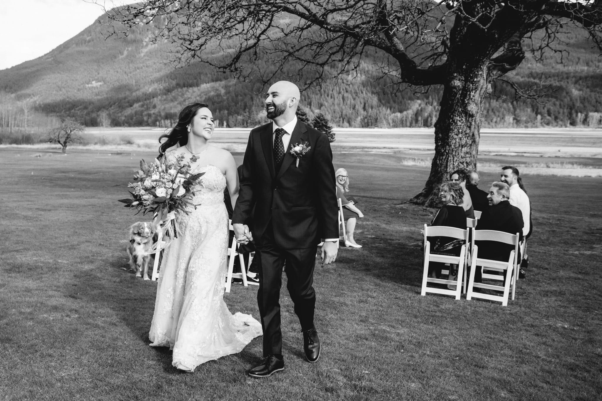 Black and white wedding photography of the bride and groom walking up a grassy aisle