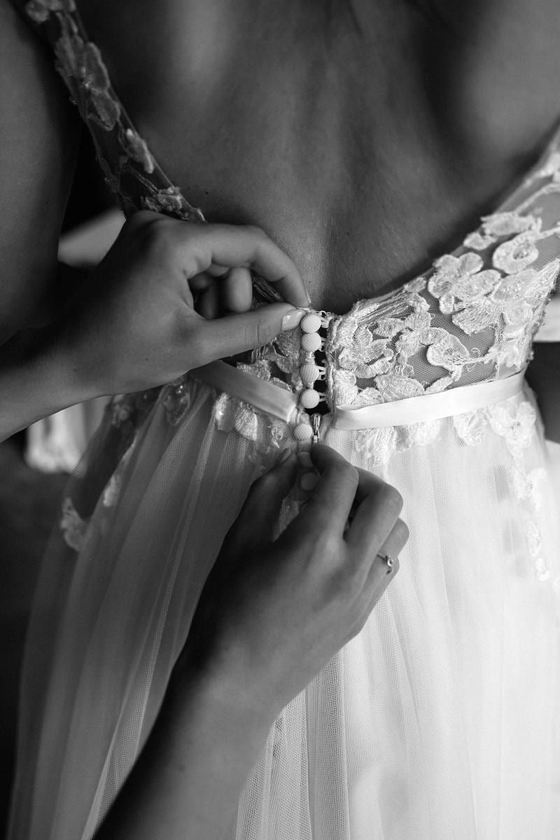 Wedding gown photoshoot, black-and-white close-up of the buttons being fastened on the bride's lace gown