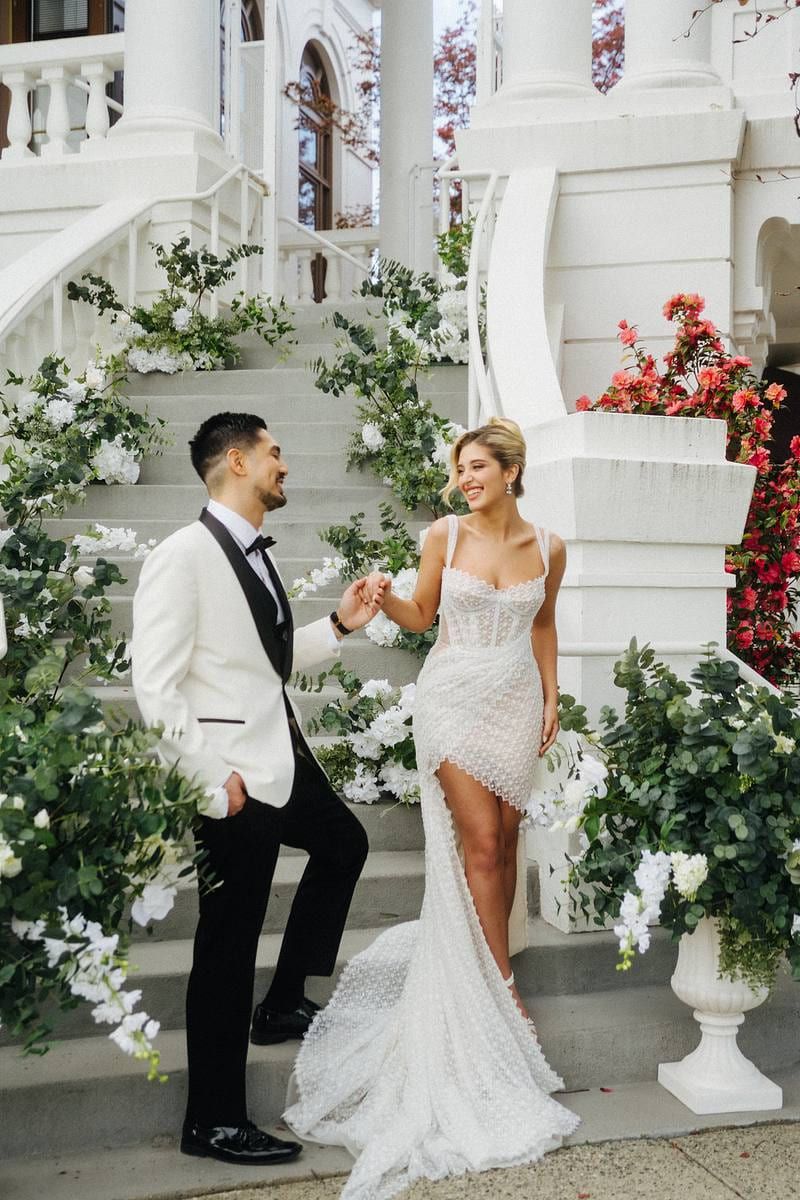 Moody wedding photography, bride and groom on the steps of a white heritage house framed with flowers