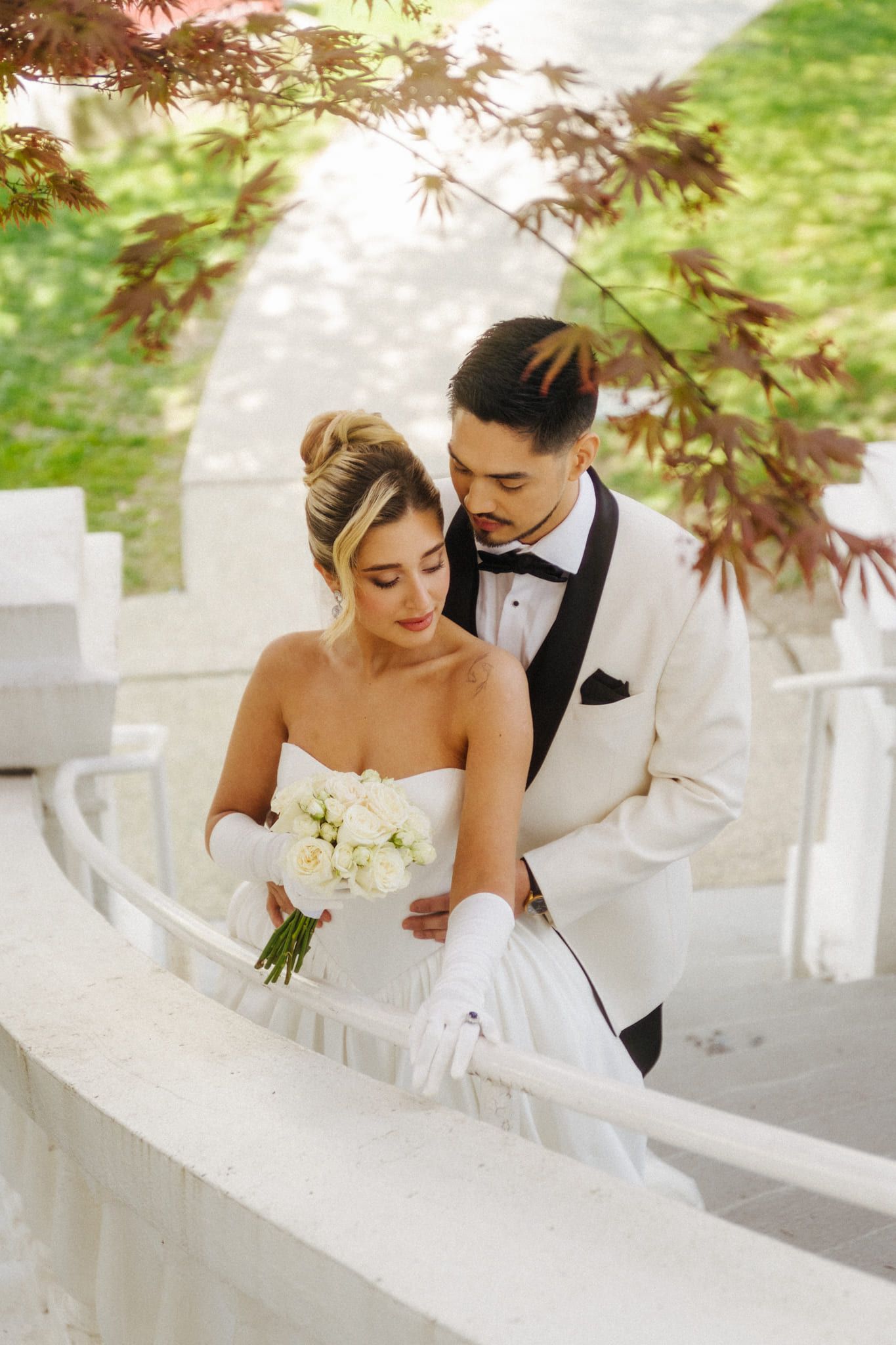 Intimate wedding photoshoot, groom in a white tuxedo holding the bride on a curved white staircase