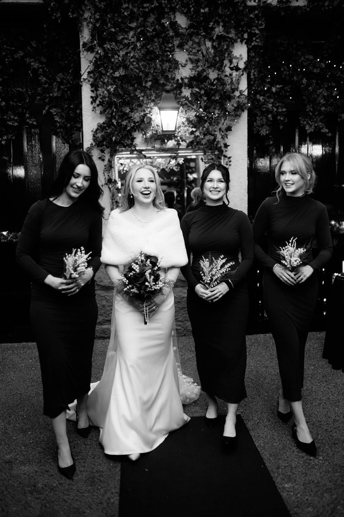 Black and white wedding photo of the bride with bridesmaids in black holding dark bouquets
