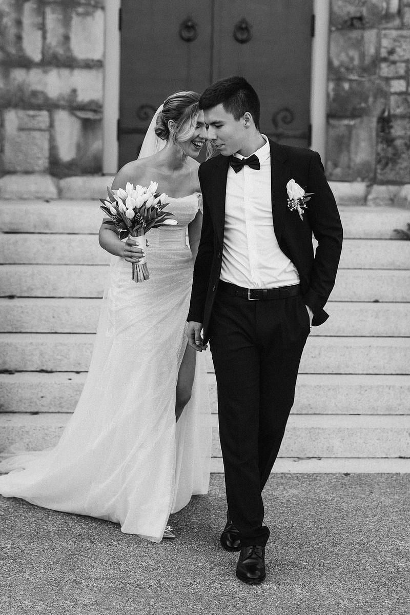 Intimate wedding photoshoot, black-and-white photo of the couple walking down stone steps, bouquet in hand