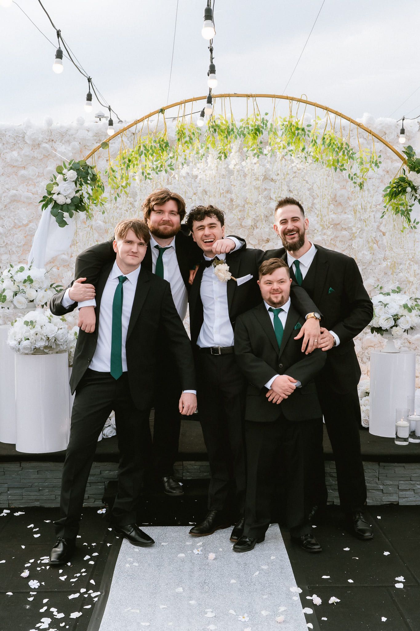 Professional wedding pictures, groom and groomsmen in front of a white flower arch