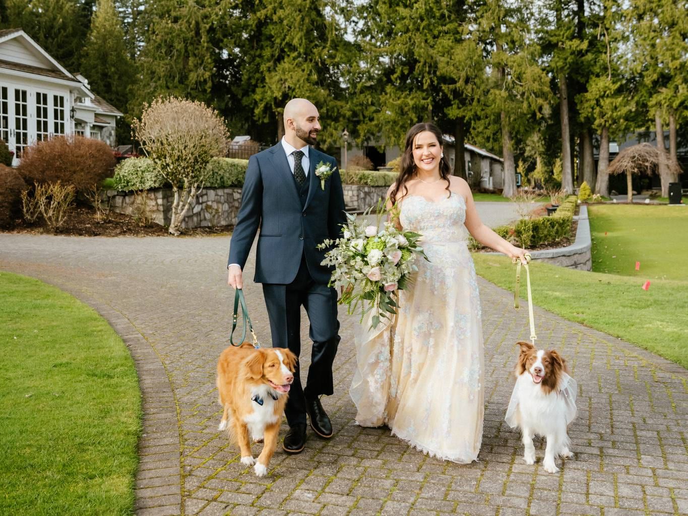 Bride and groom walking their two dogs along a paved path at a garden venue