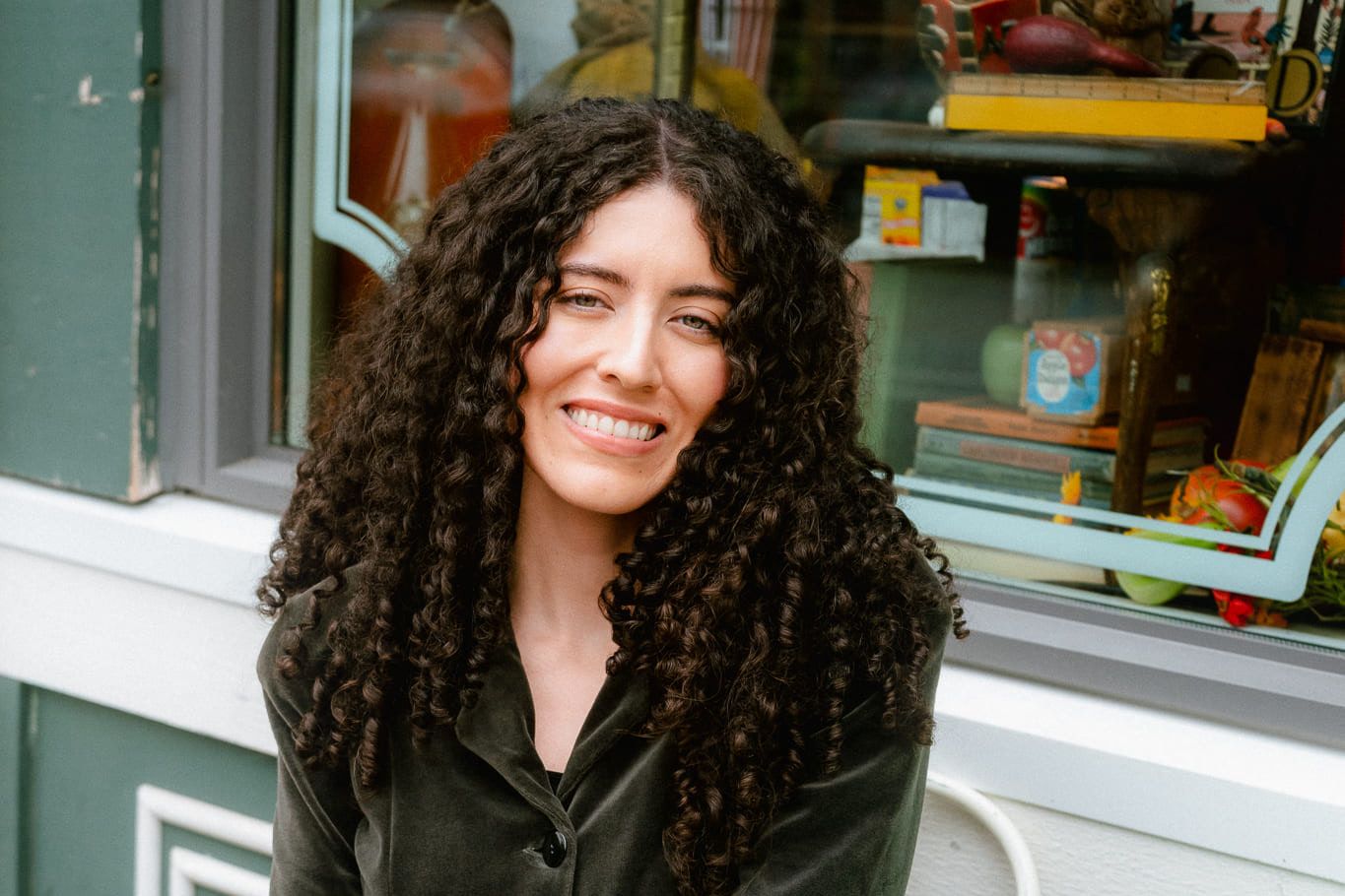 Outdoor corporate photoshoot, woman with curly hair smiling outside a café window