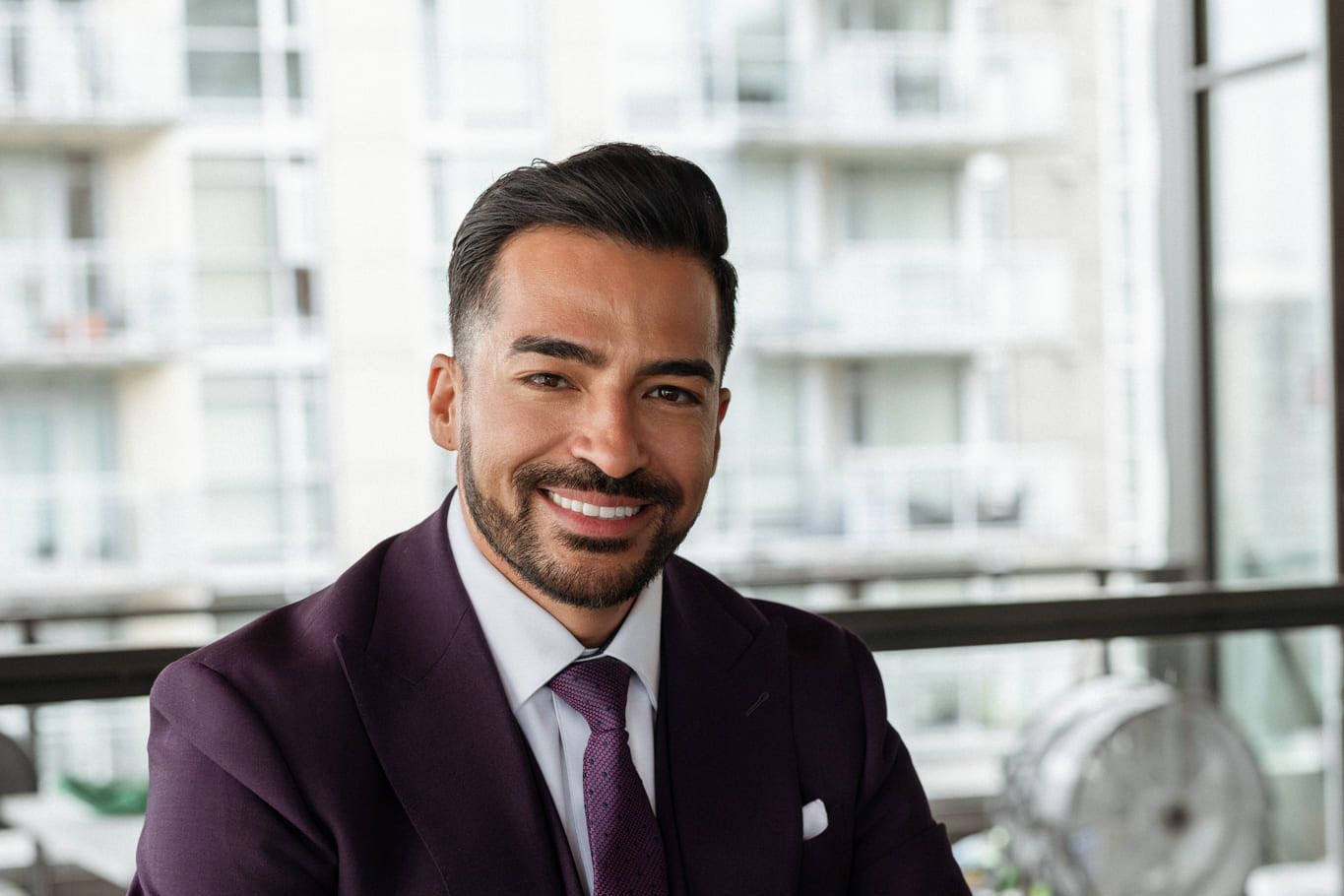 Small business branding photography, smiling man in a plum suit and tie seated by an office window