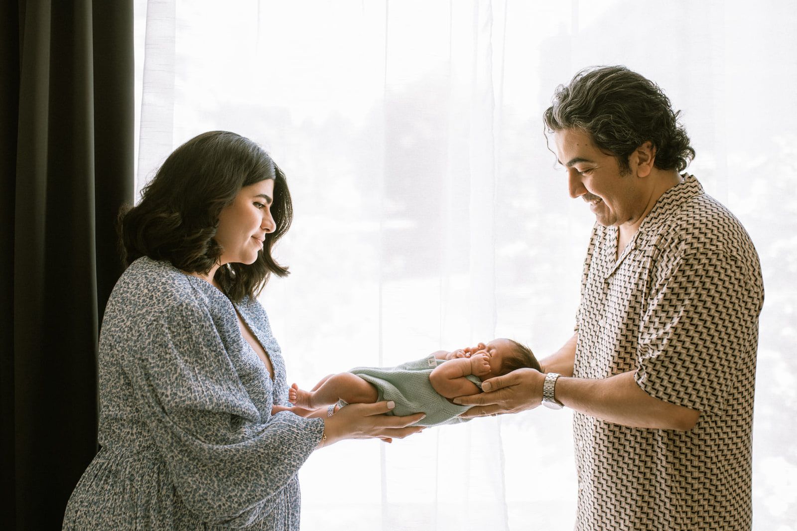 Newborn family photography in soft window light, parents holding their newborn between them