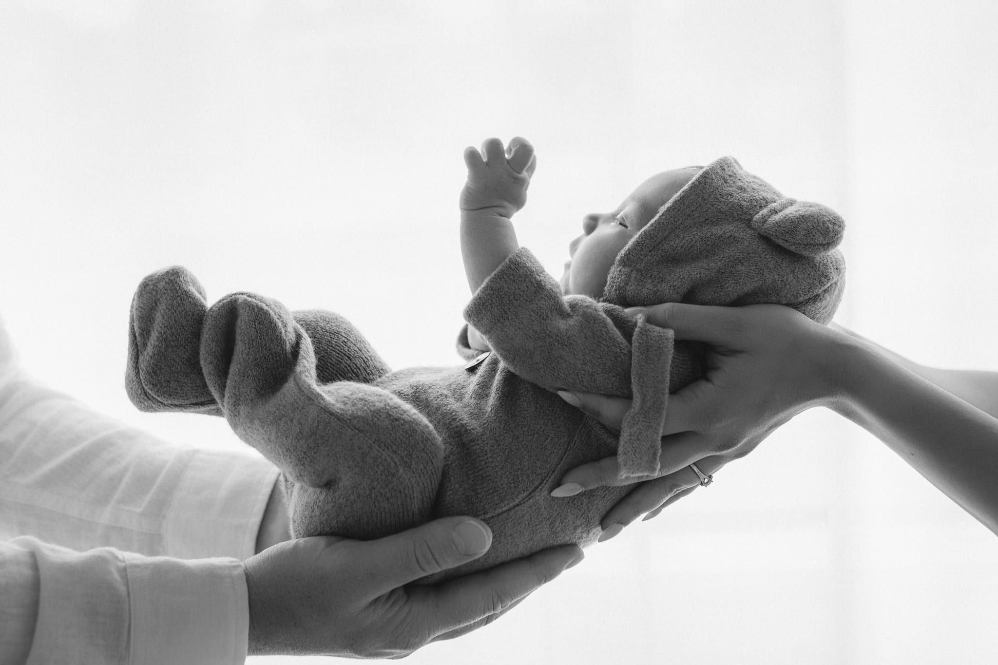 Indoor newborn photography against a bright window, newborn held up in a parent's hands, in black and white