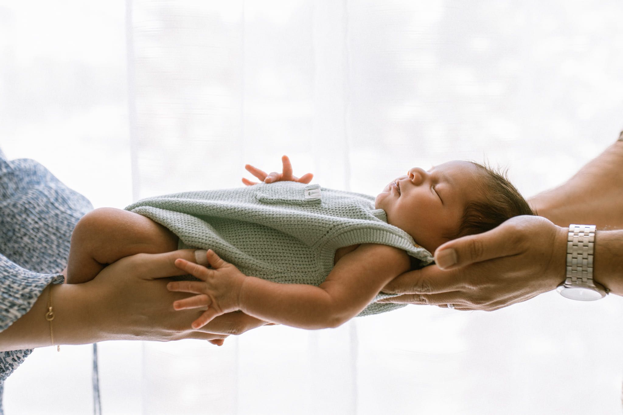 Newborn photography in Langley, newborn lying across his parents' hands by a bright window