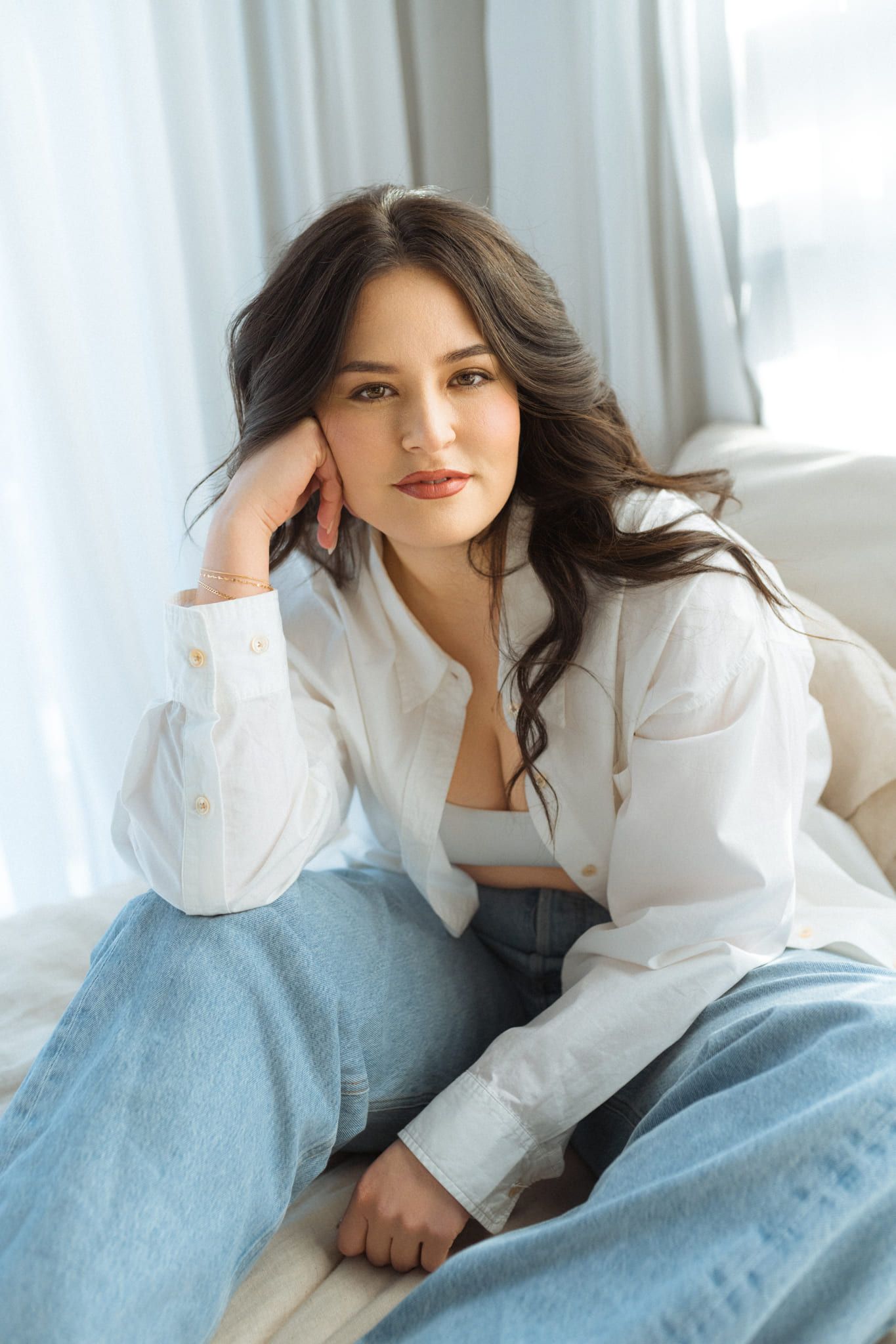 Portrait photoshoot by a bright window, woman sitting in jeans and a white shirt