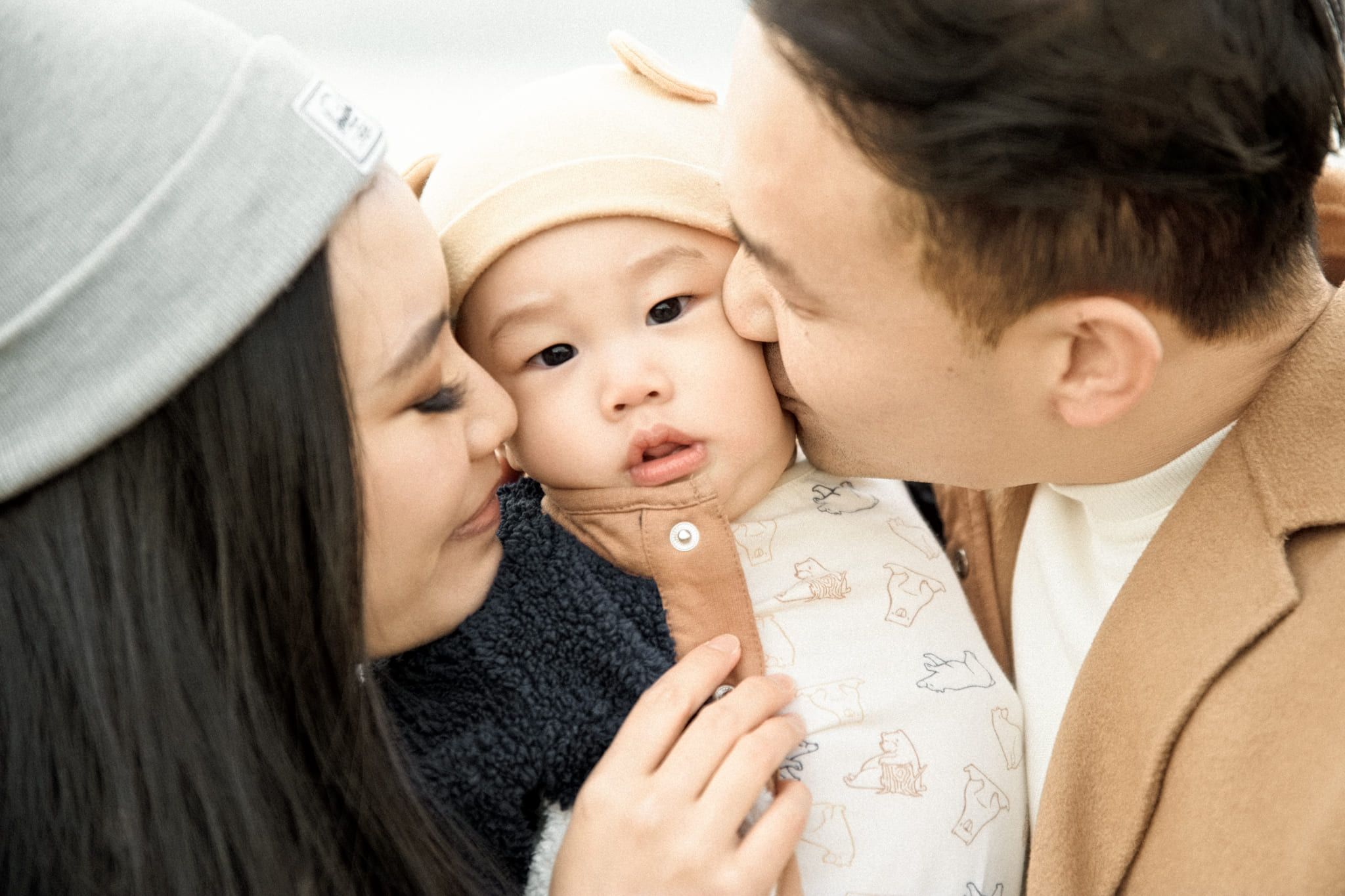 Family photos in winter, parents in winter hats kissing their baby's cheeks