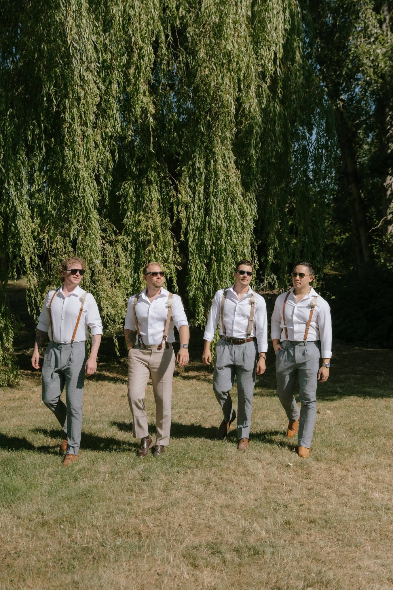Groom and groomsmen in suspenders walking across the lawn