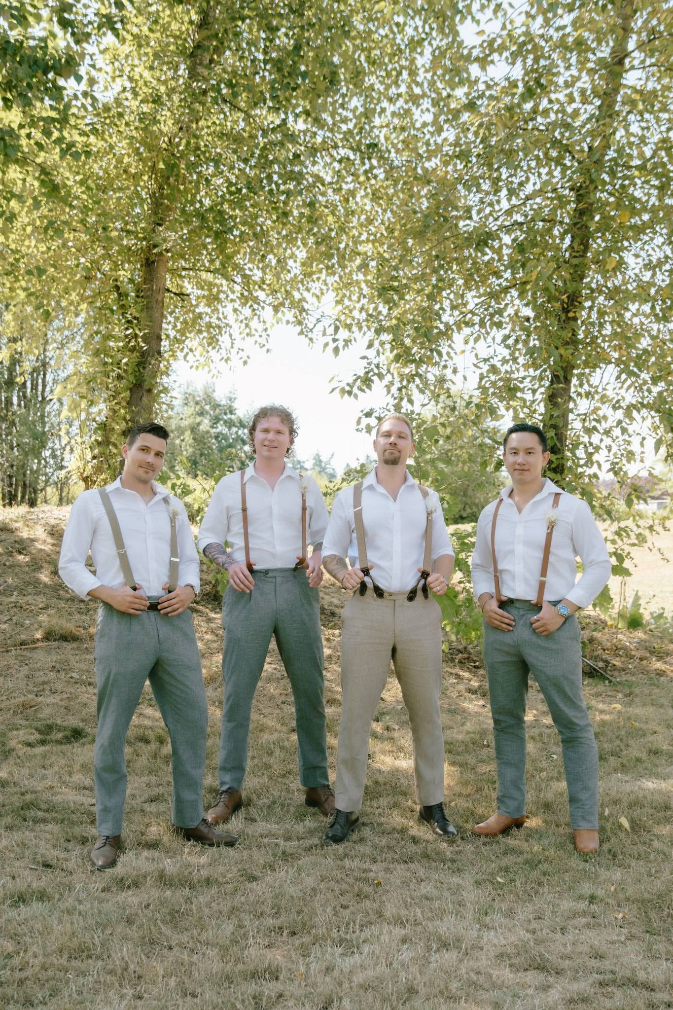 Groom and groomsmen in suspenders posing beneath the trees
