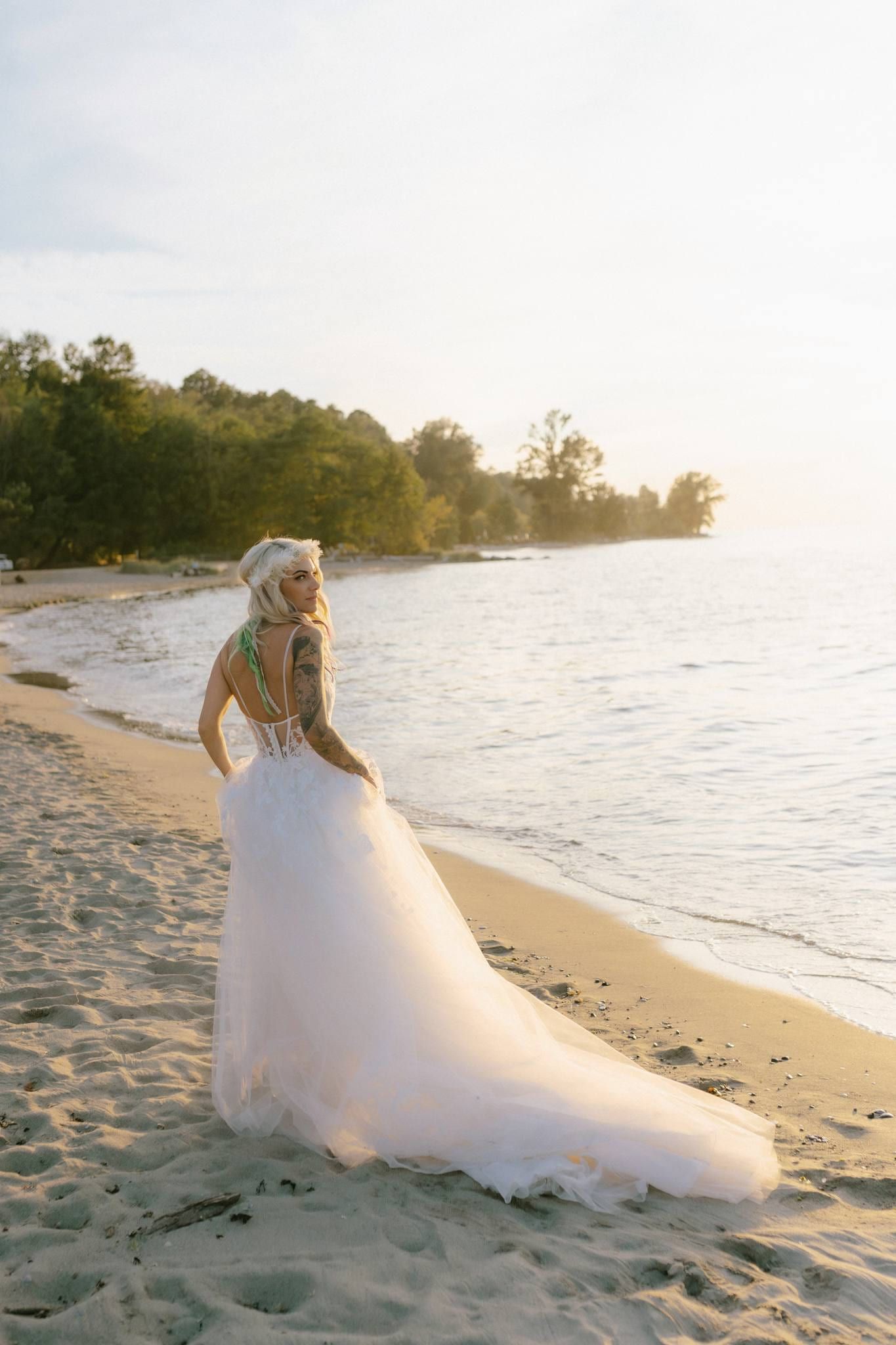 Bride walking along the shore at sunset with her train trailing