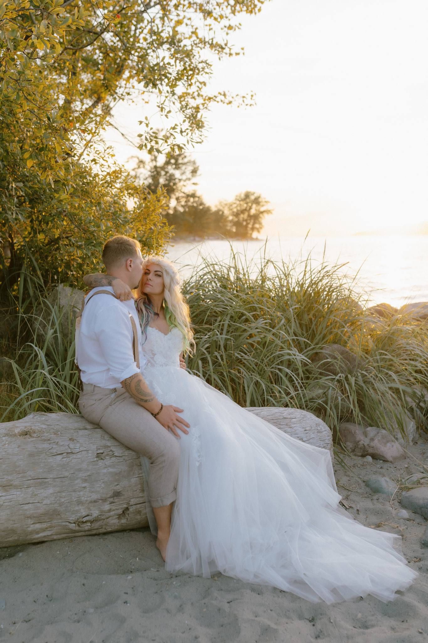 Couple seated on a driftwood log at the beach at sunset