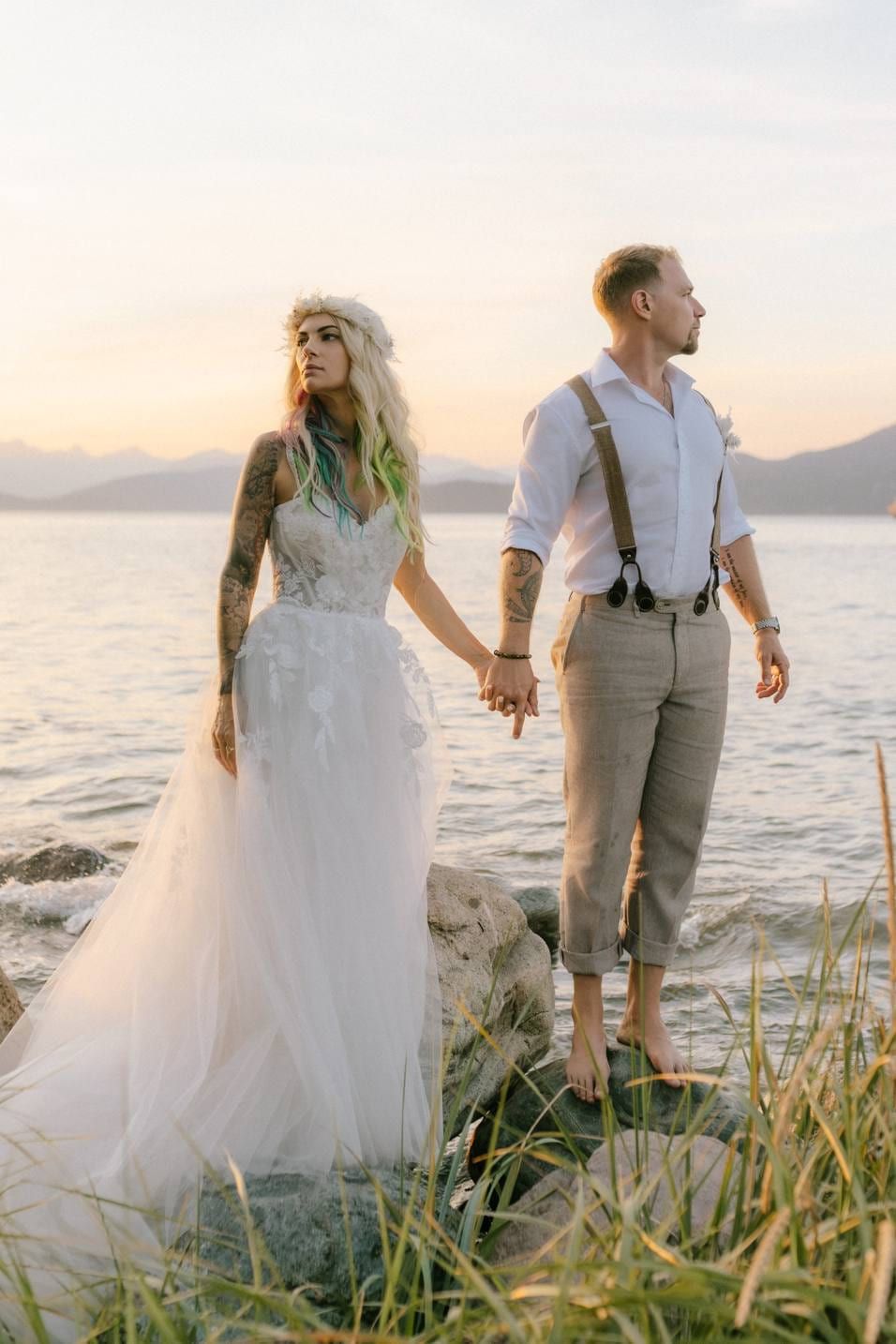 Bride and groom holding hands on rocks by the sea at sunset