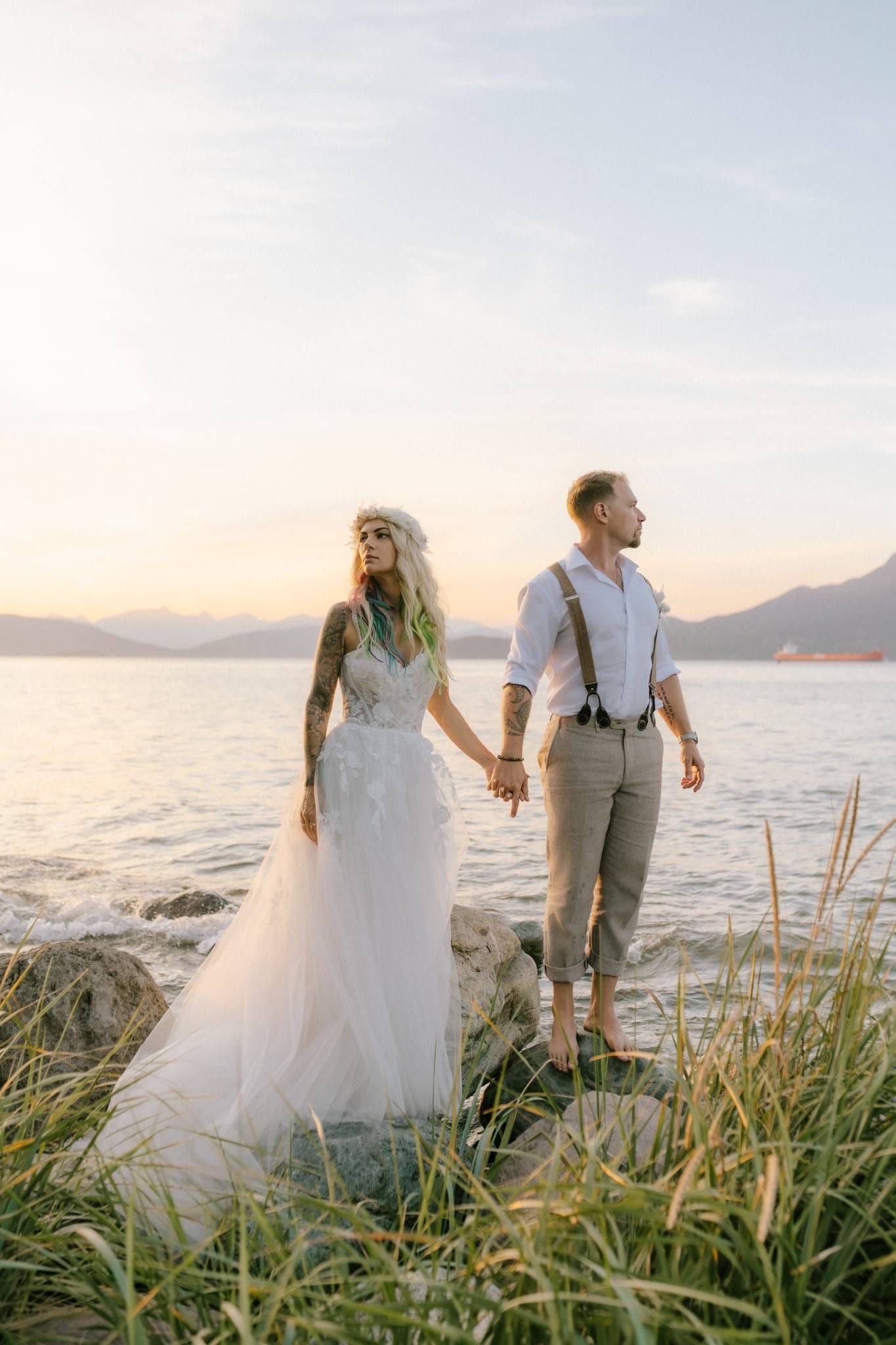 Couple holding hands on the rocks by the sea at sunset
