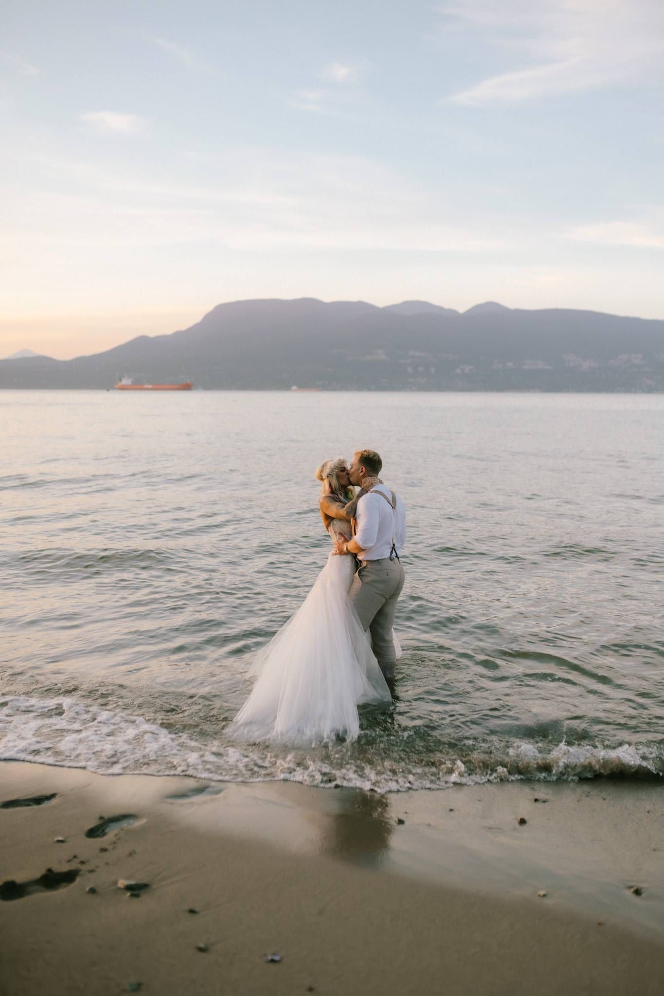 Couple standing in the shallows at sunset with mountains behind