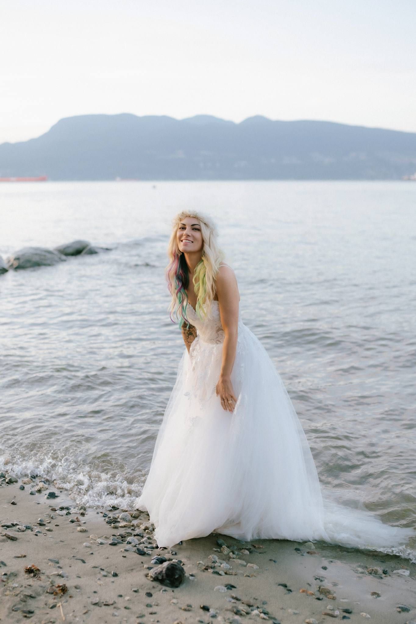 Bride standing in the water at sunset, mountains behind