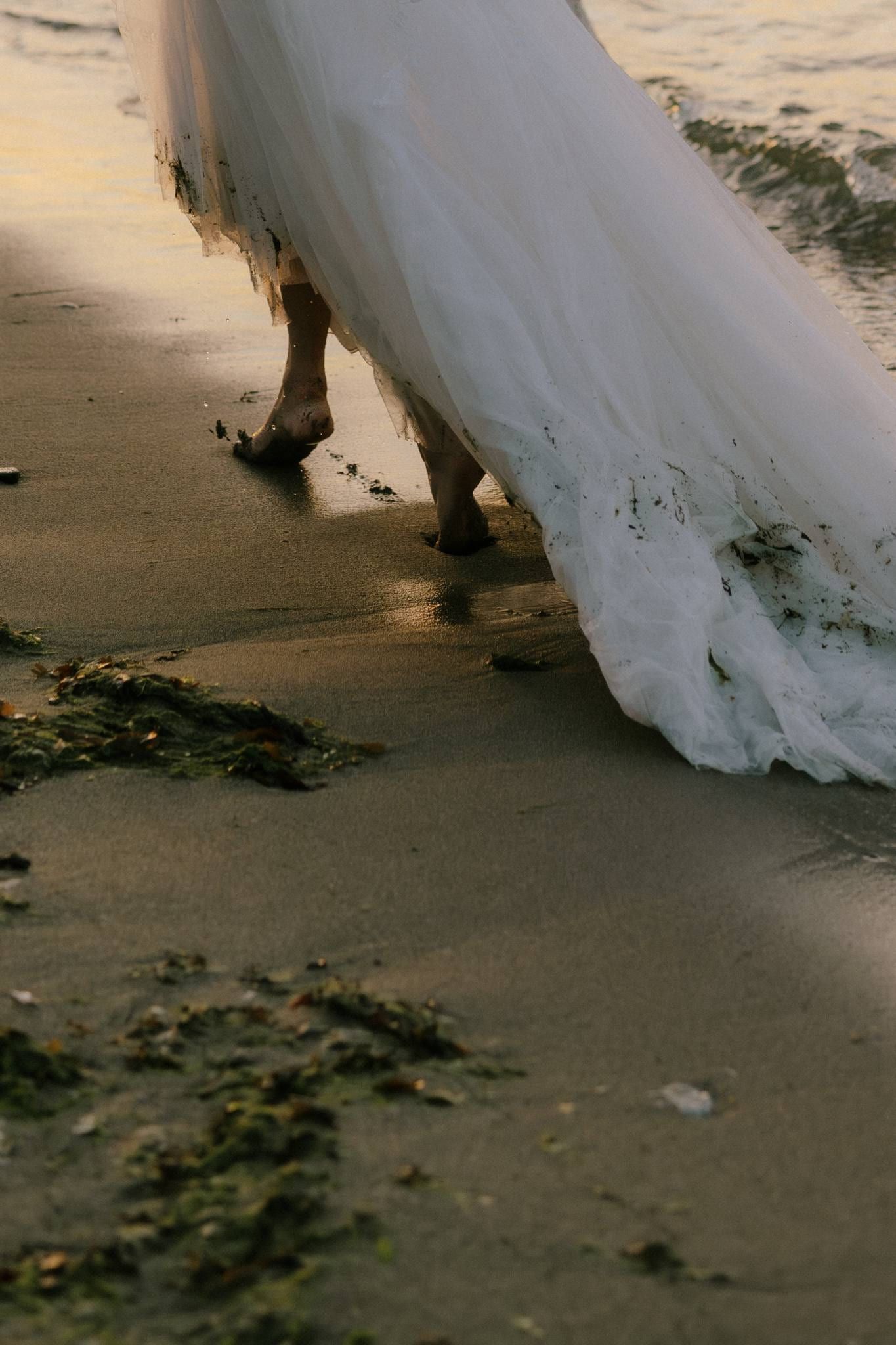 Close-up of the bride's lace hem trailing across the sand