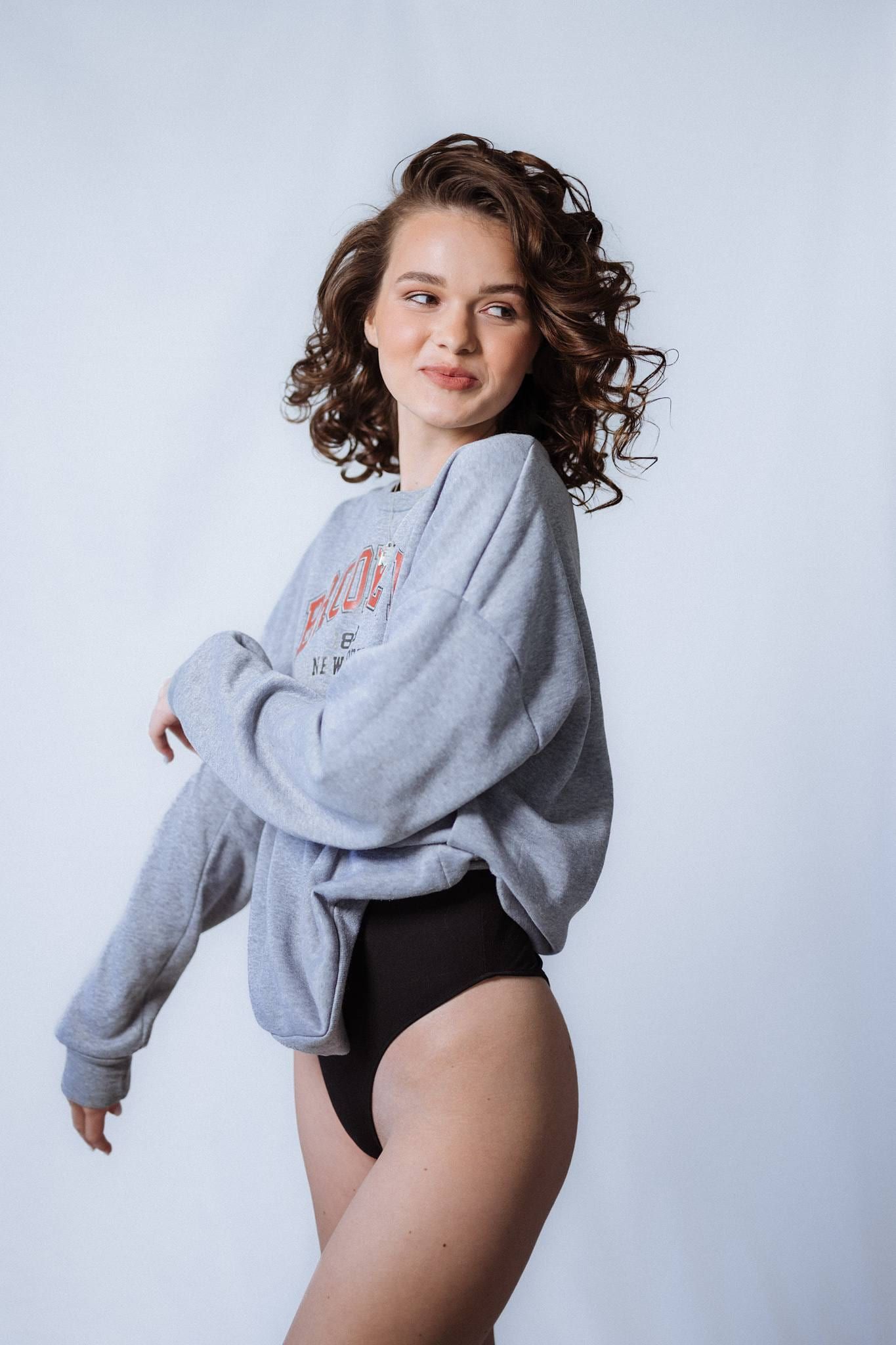 Model in a grey sweater and black bodysuit seated on a white studio block